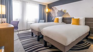 A hotel room with two beds, a desk, a chair, and a small table. - Novotel Strasbourg Centre Halles (Strasbourg)