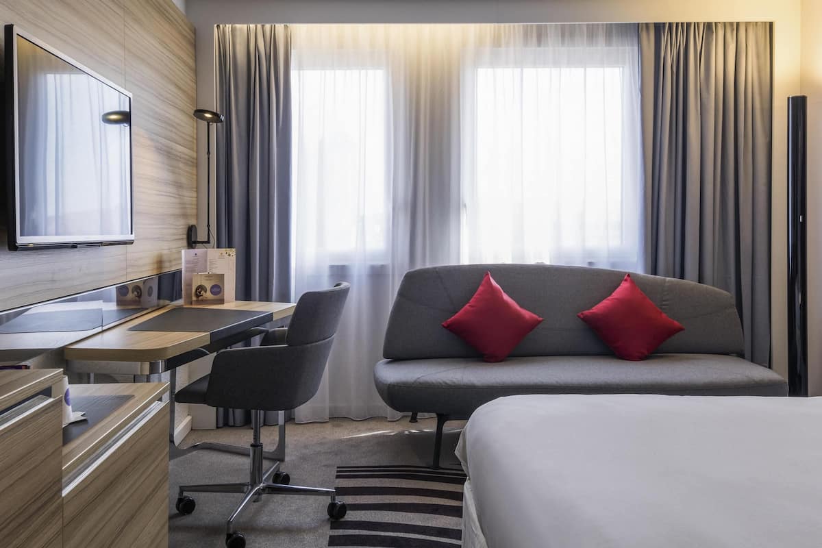 A hotel room with a bed, a desk with a chair, a TV, and curtains.