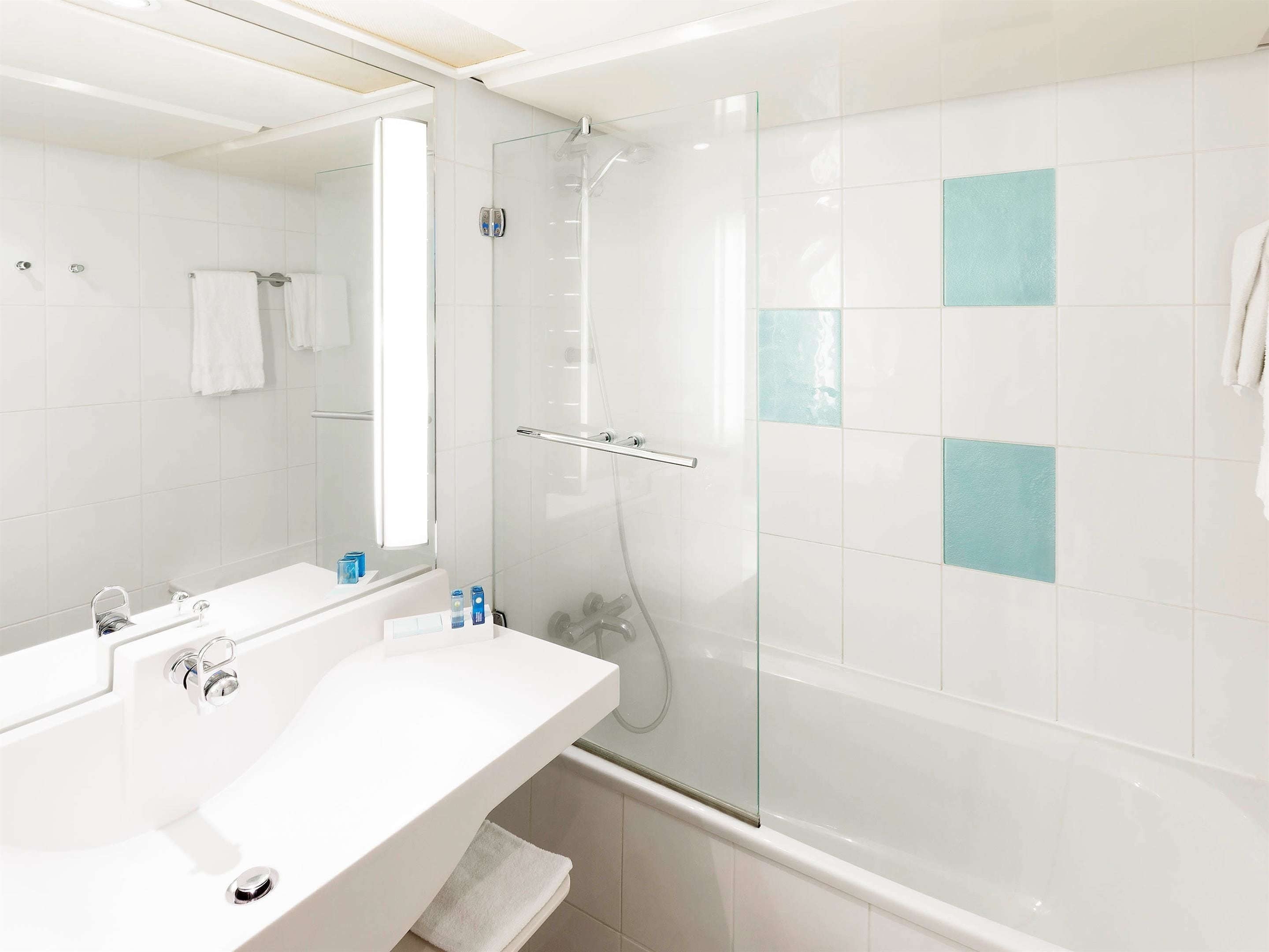 A modern bathroom with a glass-enclosed shower, a white sink with a mirror, and a tiled wall with blue accents.