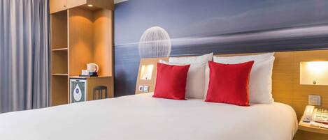 Een hotelkamer met een groot bed, rode en witte kussens, een nachtkastje met een telefoon en een wandlamp.