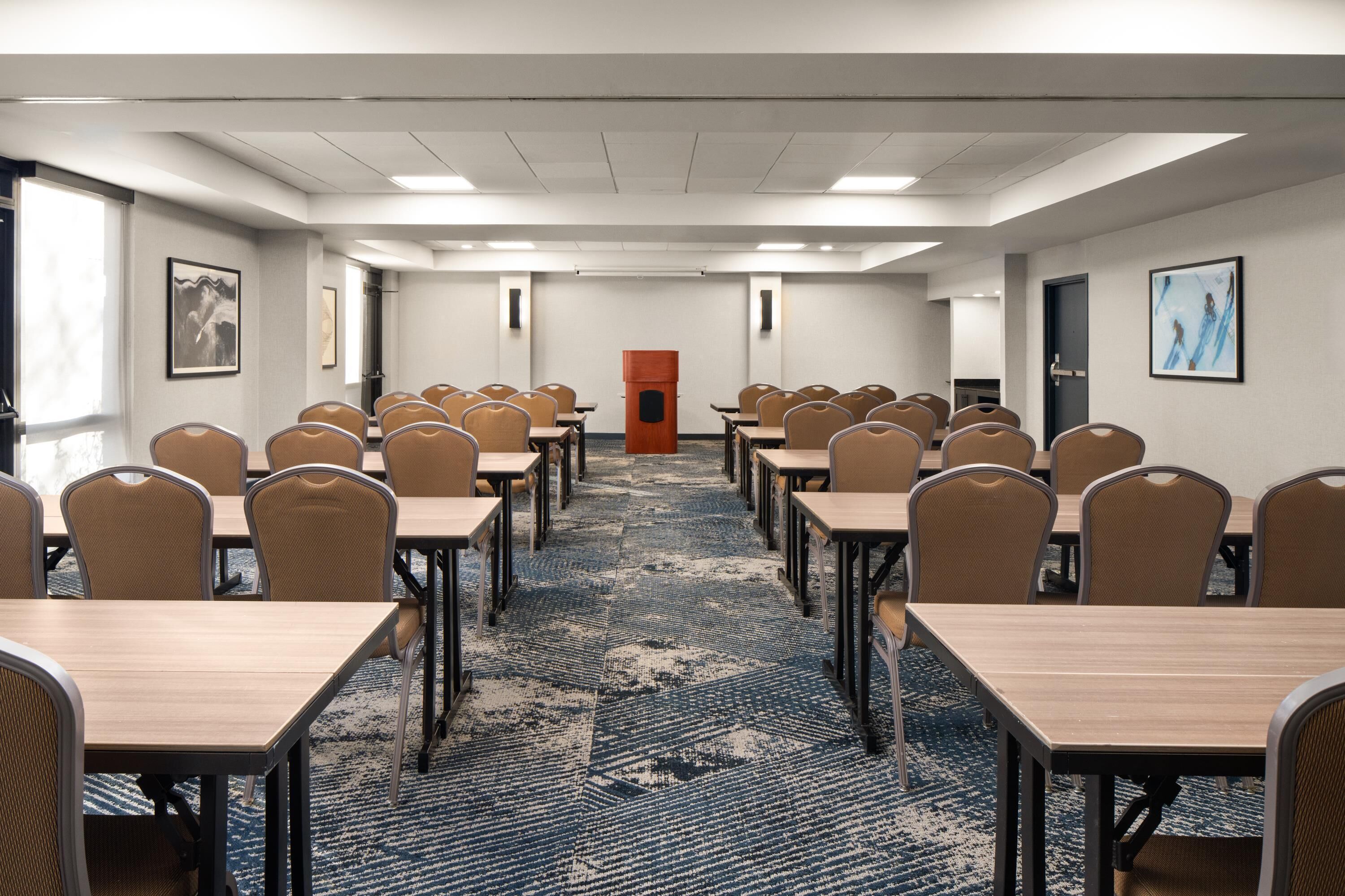 A conference room with rows of tables and chairs, a carpeted floor, and a door at the far end.
