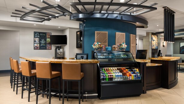 Zona de bar con mostrador curvo, taburetes, refrigerador para bebidas y una pantalla de televisión.