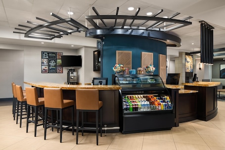 A bar area with a curved counter, stools, a beverage cooler, and a television screen.