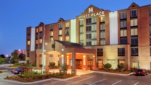 Un hotel de varios pisos con un cartel llamativo de "Hyatt Place", una entrada cubierta y un estacionamiento.