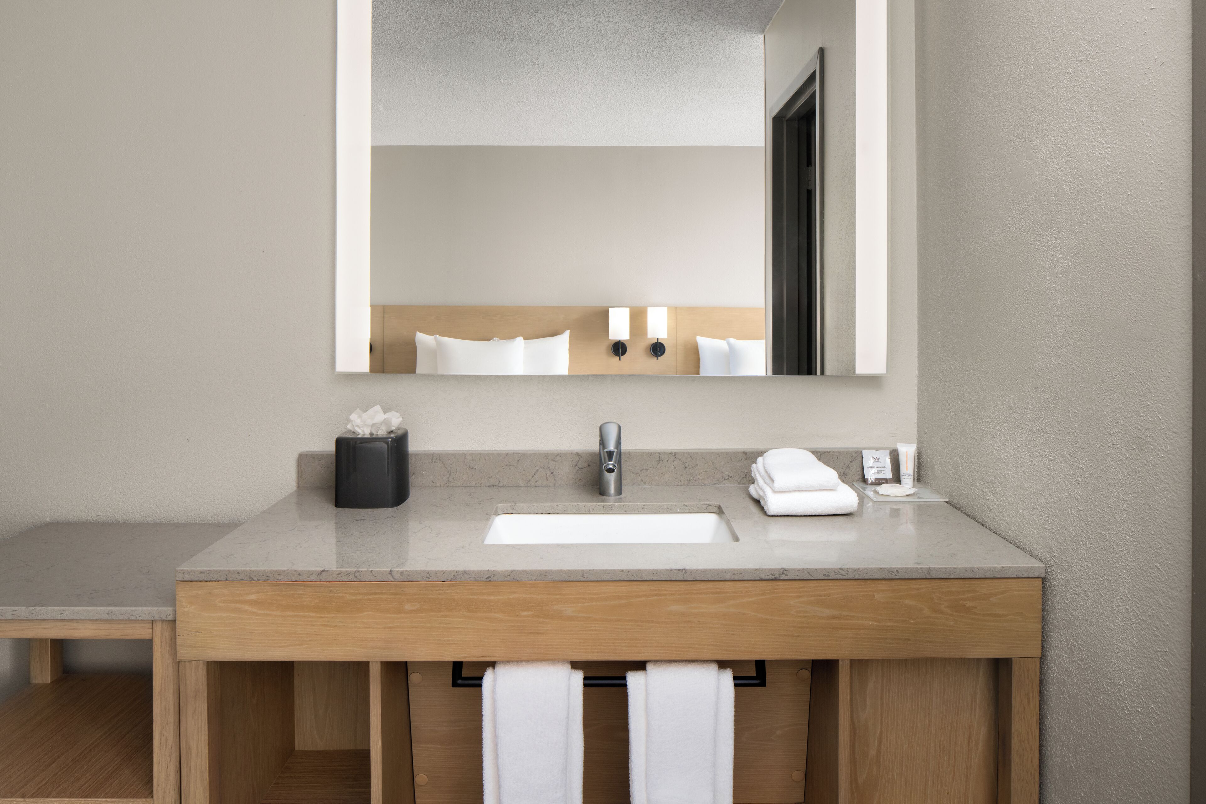 A modern bathroom with a wooden vanity, a large mirror, and a built-in sink.
