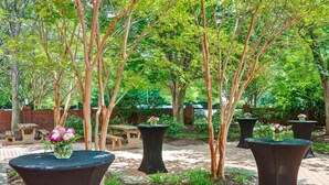 Un patio al aire libre con mesas redondas, bancos y árboles.