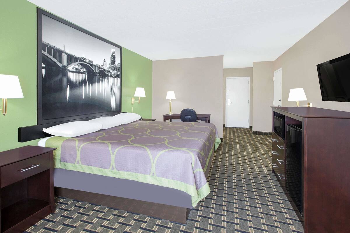A hotel room with a bed, two bedside tables, a television, a desk, and a chair.