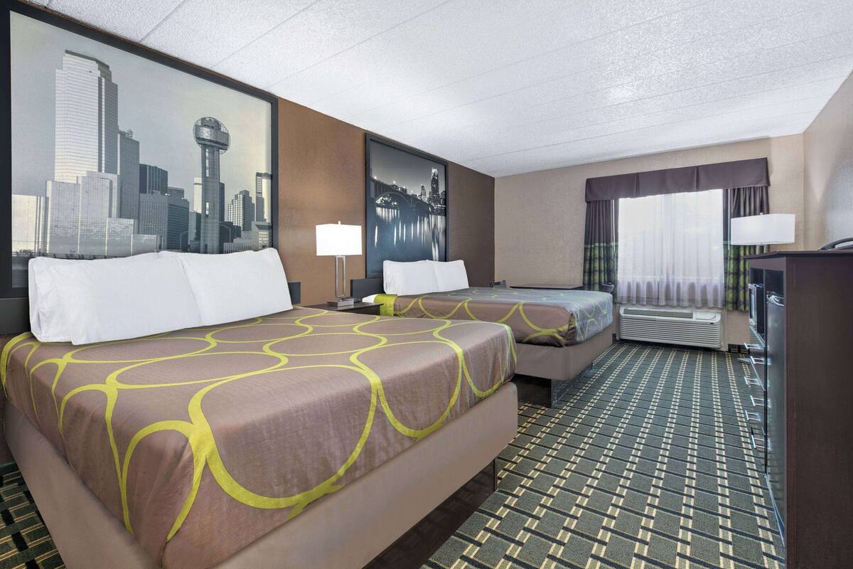 A hotel room with two beds, a desk, and a window with curtains.
