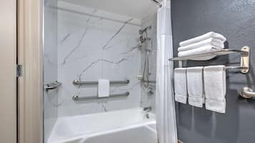 A modern bathroom with a glass-enclosed shower, a white bathtub, and a towel rack with folded towels.