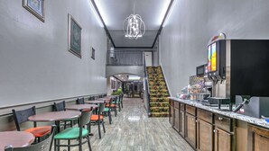 Un restaurante con una barra larga, varias mesas y sillas. Se ve una escalera que sube a un nivel superior.