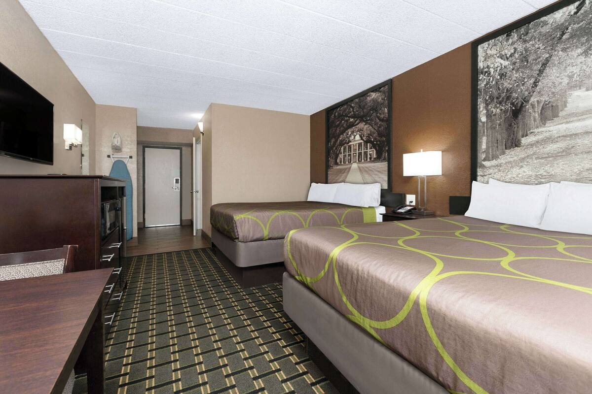 A hotel room with two beds, a TV, a desk, and a patterned carpet.
