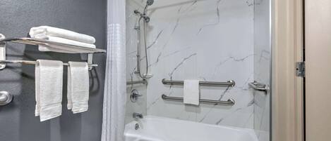 A modern bathroom with a bathtub, a shower with a handheld showerhead, and a towel rack with multiple towels.