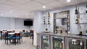 A bar area with a refrigerated display case, shelves with bottles, and a television on the wall. - AmericInn by Wyndham Woodstock IL (Woodstock)