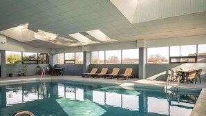 An indoor swimming pool with clear blue water, sunlit windows, and lounge chairs. - AmericInn by Wyndham Woodstock IL (Woodstock)