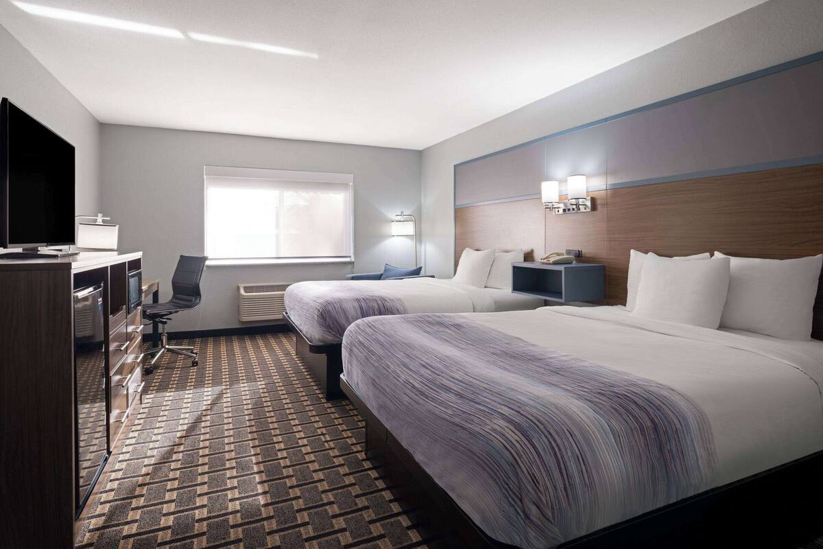 Hotelkamer met twee bedden, een bureau, een flatscreen televisie, een stoel, een raam met zonwering en een wandlamp.