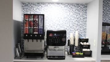 Una estación de bebidas de autoservicio con una máquina de café, un dispensador de jugo y un dispensador de agua.
