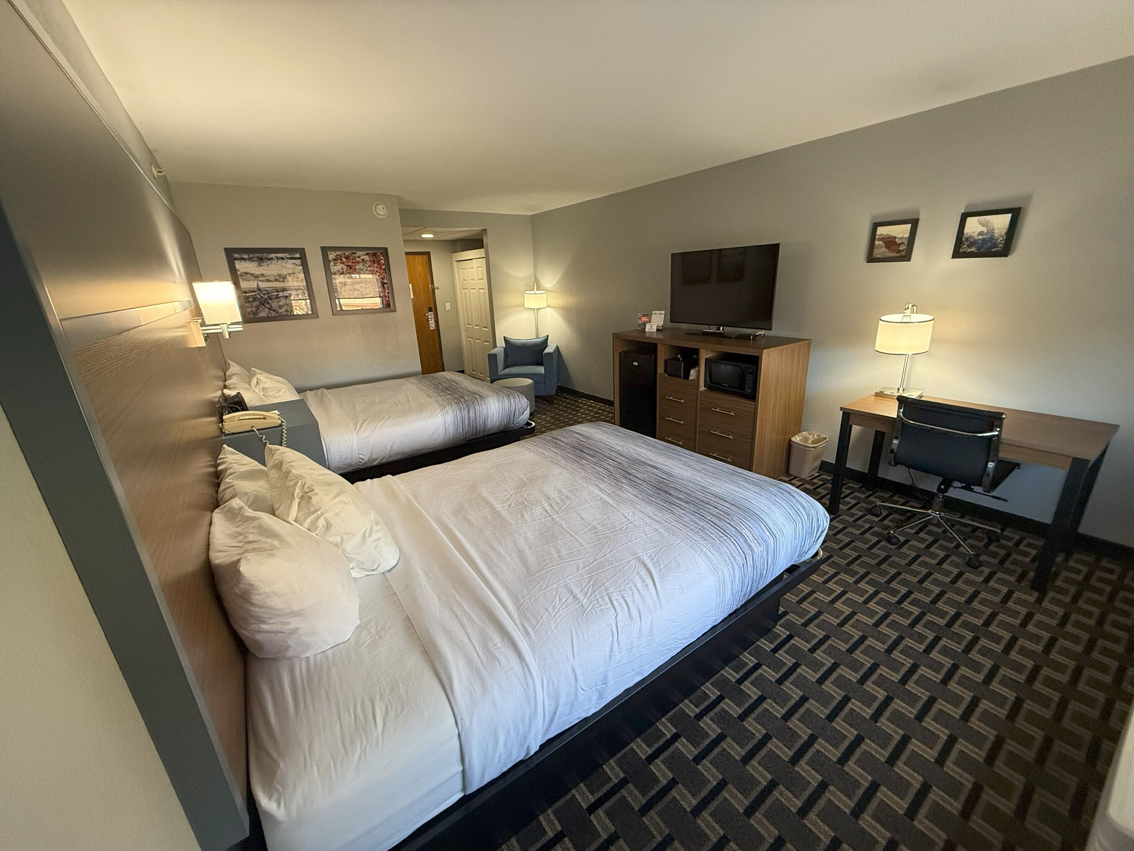 A hotel room with two beds, a desk with a chair, a television, and a small table with a lamp.