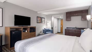 A hotel room with a large bed, a television, a microwave, a desk, a chair, and a kitchenette.