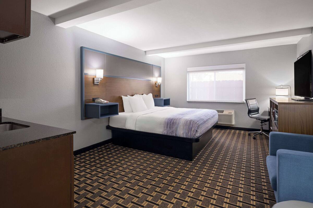 Een hotelkamer met een bed, een bureau, een stoel, een televisie en een raam met jaloezieën.