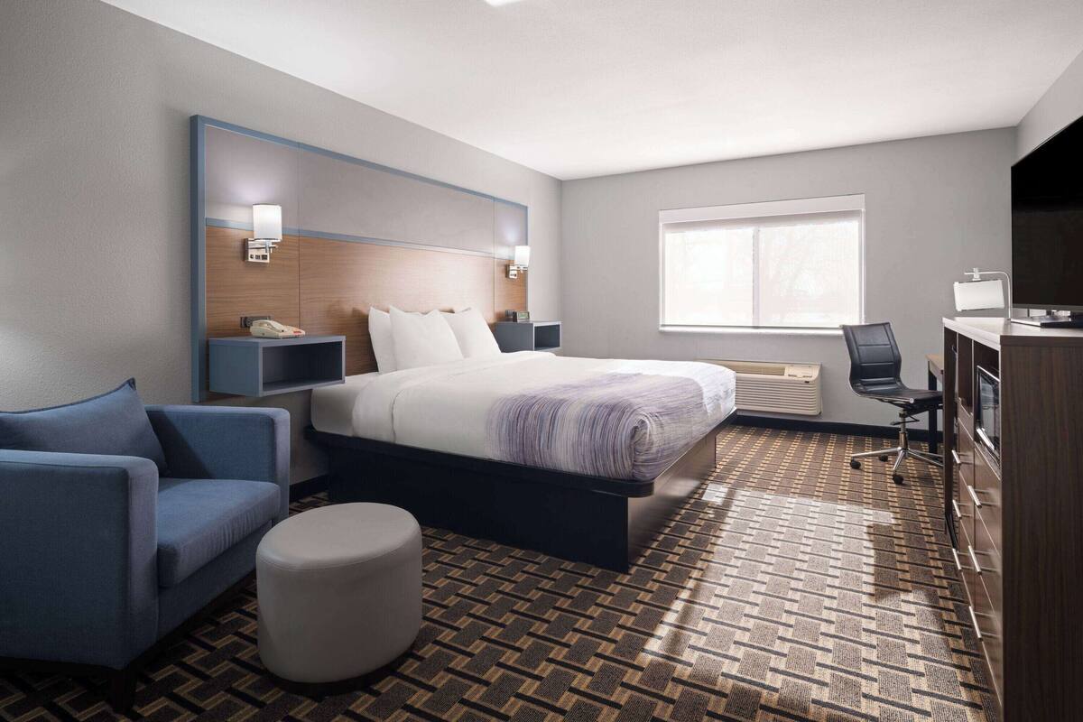 Een hotelkamer met een bed, een bureau, een stoel, een bank en een klein voetenbankje.