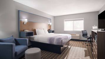 A hotel room with a bed, a desk, a chair, a sofa, and a small ottoman.