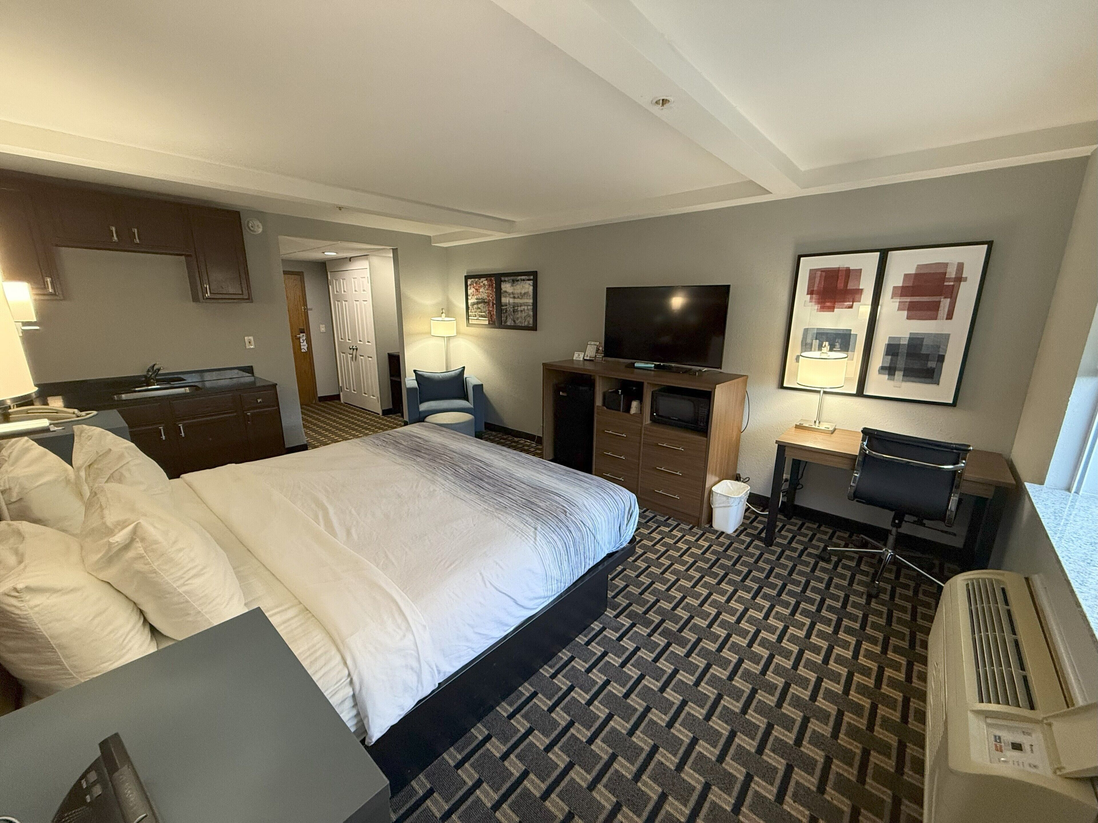 Een hotelkamer met een groot bed, een bureau, een televisie, een stoel, een bureaulamp en een prullenbak.