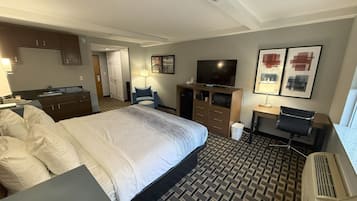 Een hotelkamer met een groot bed, een bureau, een televisie, een stoel, een bureaulamp en een prullenbak.