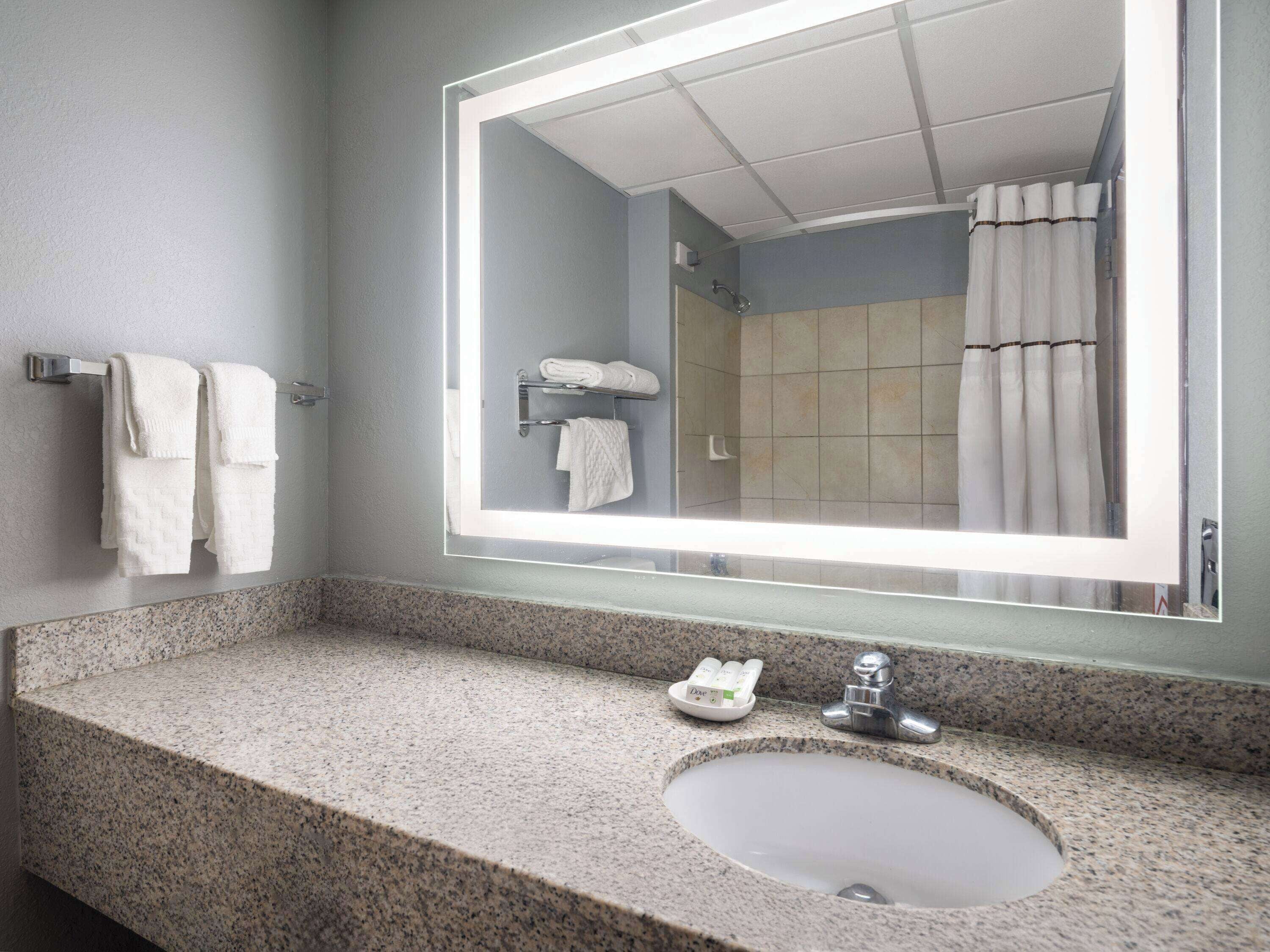 Un baño con encimera de granito, un lavamanos, un espejo y una cortina de ducha.