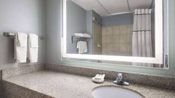 Un baño con encimera de granito, un lavamanos, un espejo y una cortina de ducha.