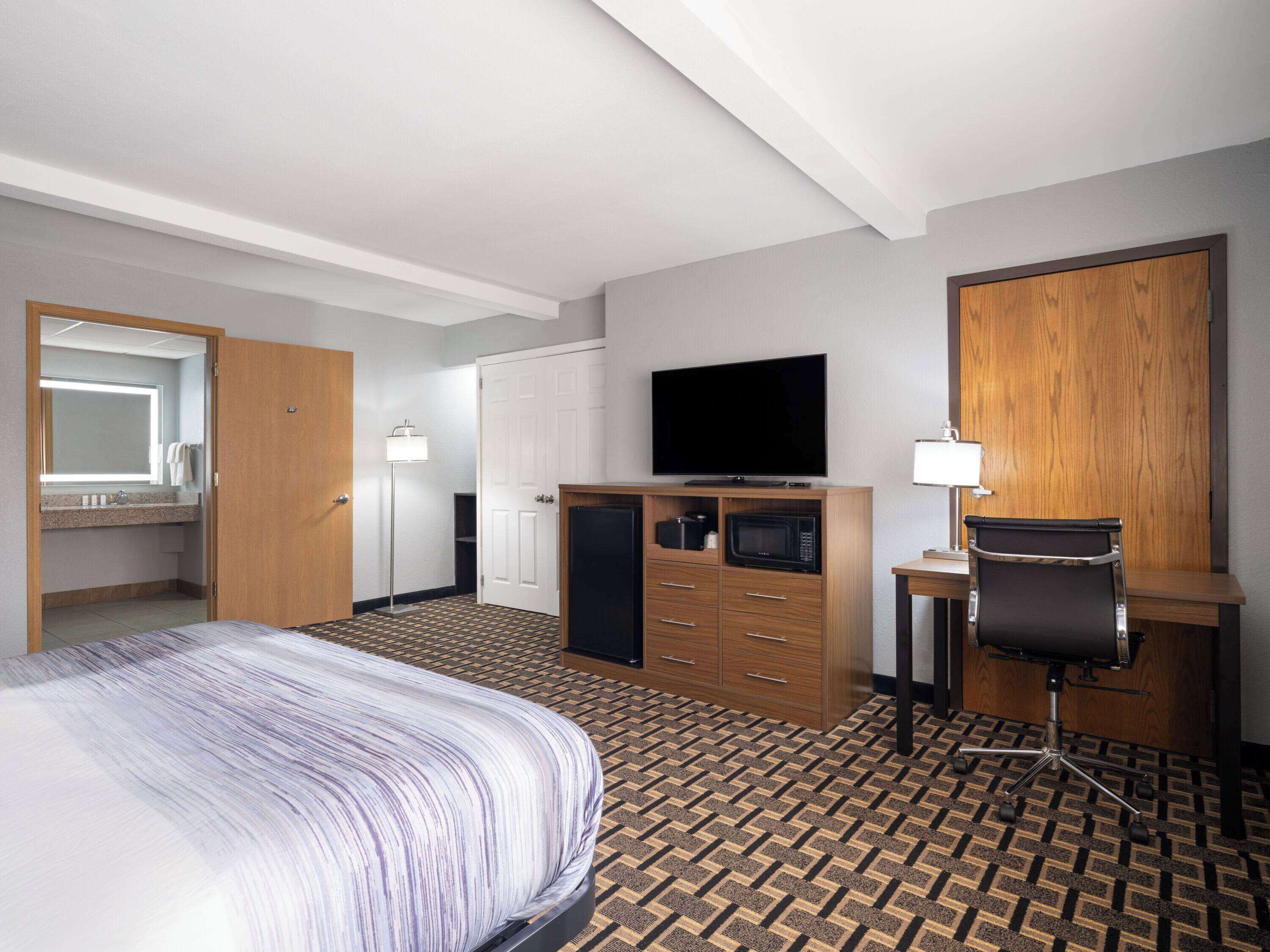 A hotel room with a bed, a desk with a chair, a television, a microwave, and a wardrobe.