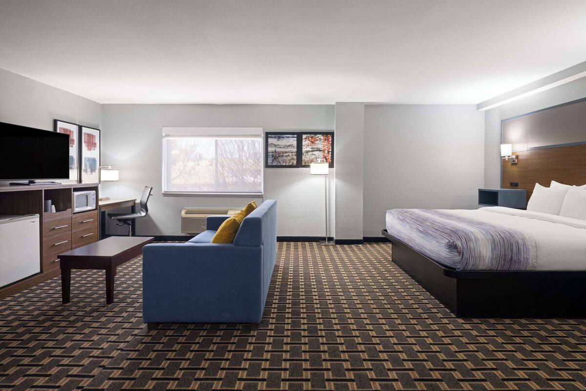 Een hotelkamer met een bed, een slaapbank, een bureau met een televisie, een raam en een wandlamp.