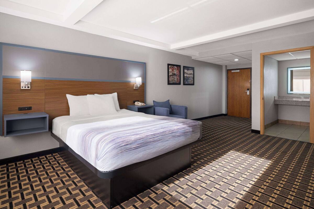 Een hotelkamer met een groot bed, nachtkastjes, een bureau en een badkamer zichtbaar door een geopende deur.