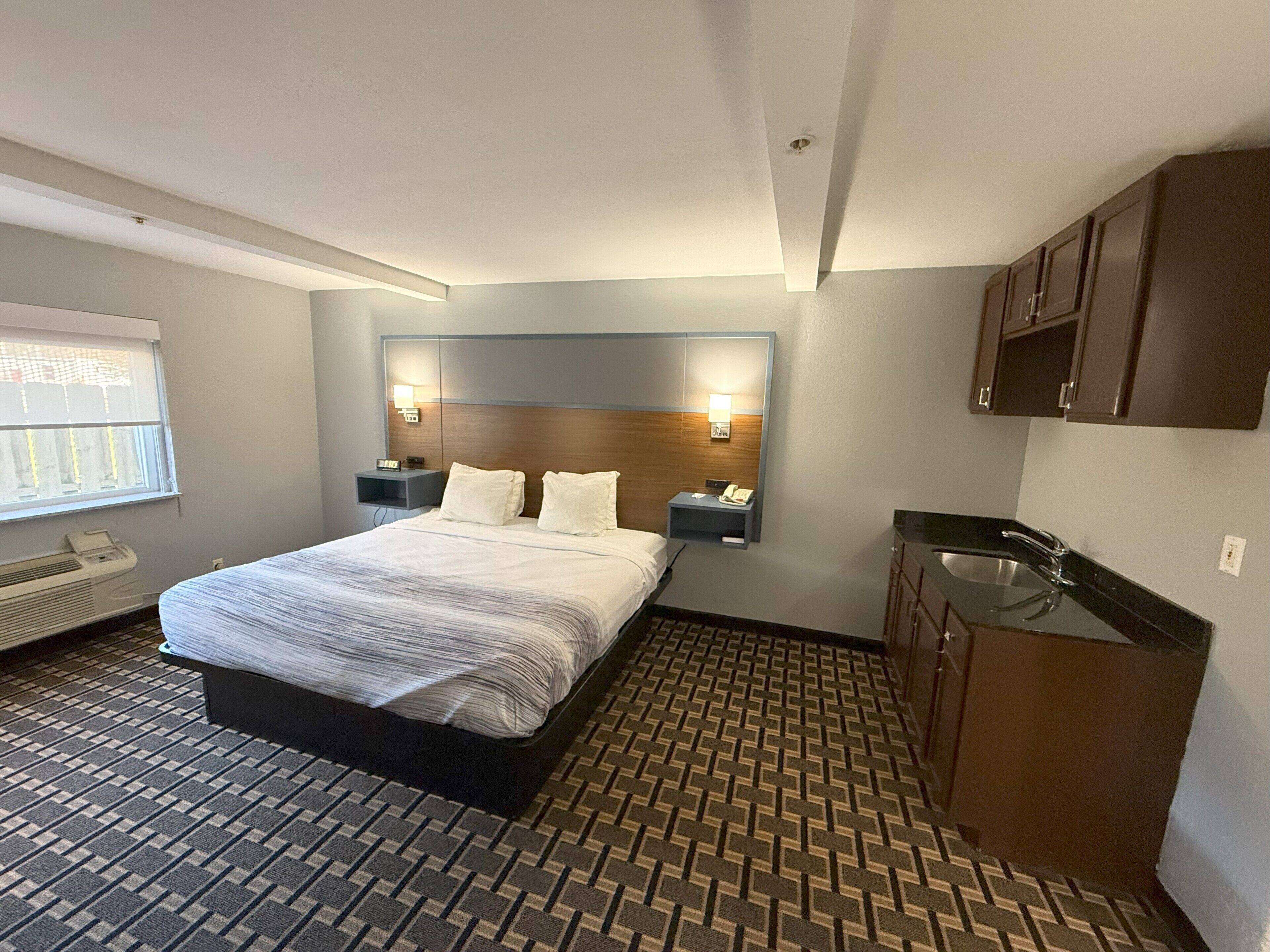 Habitación de hotel con cama, mesitas de noche, un escritorio integrado, lavamanos y ventana.