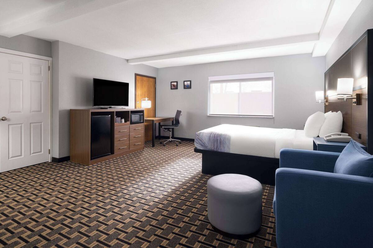 Een hotelkamer met een bed, een bureau met een televisie, een stoel, een lamp en een kamerkleed met een patroon.