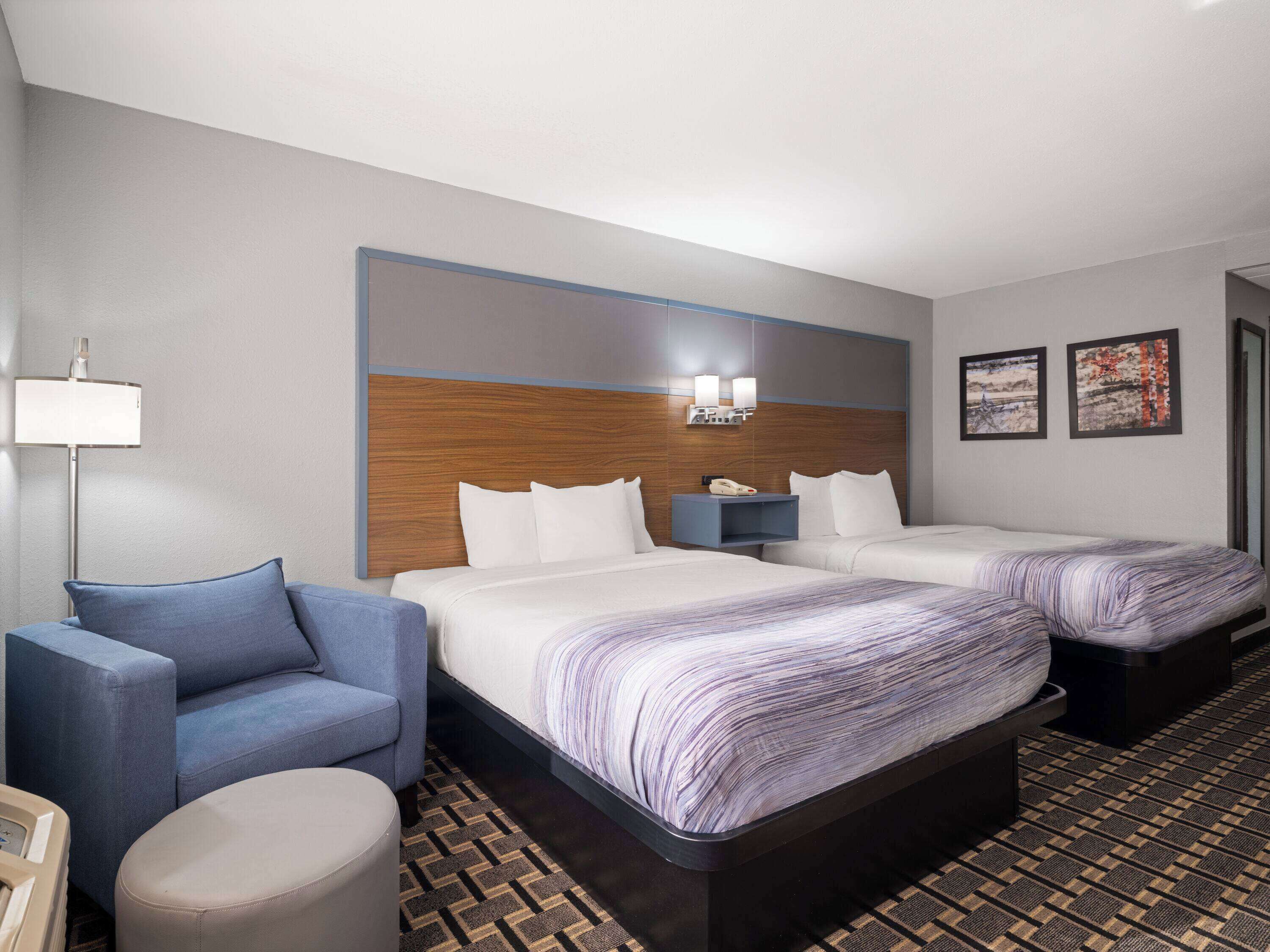 Une chambre d’hôtel avec deux lits, un bureau, une chaise et une lampe.