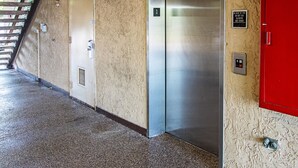 A hallway with a metallic elevator, a red door, and a fire safety sign. - Red Oak Inn Detroit - Southfield (Southfield)