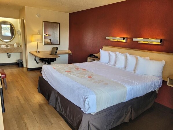 Relax in this inviting room featuring a large bed, a desk, and a chair, with a floral-patterned duvet and a telephone nearby.