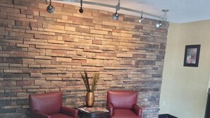 A room with a stone wall, two red leather chairs, a small table with a magazine, and a vase with dried plants. - Red Oak Inn Detroit - Southfield (Southfield)