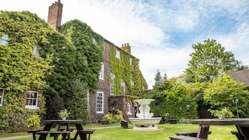 A garden with picnic tables and a fountain, surrounded by ivy-covered brick buildings.