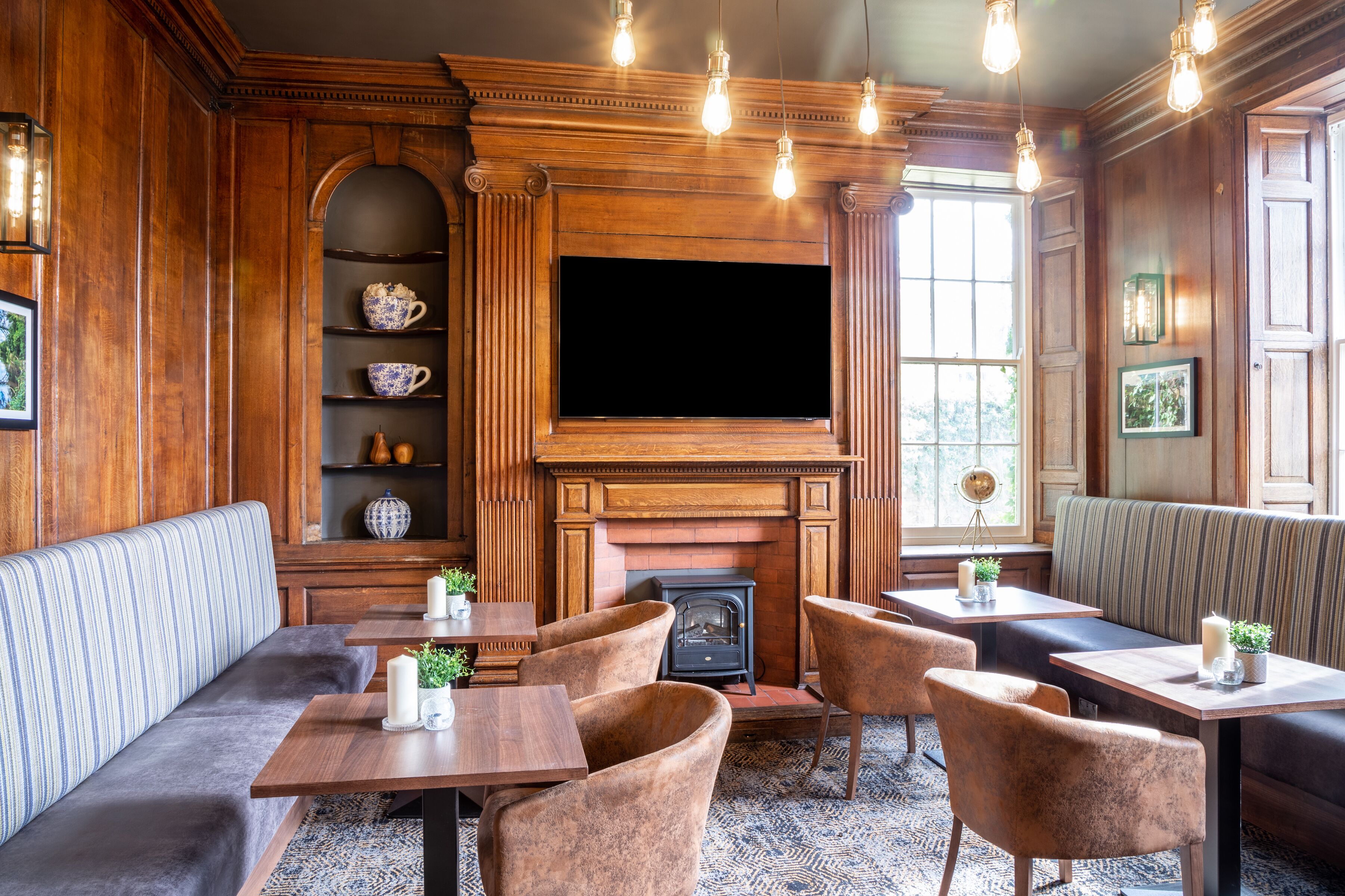 A cozy room with a fireplace, wooden paneling, and a television. There are seating areas with tables and chairs.