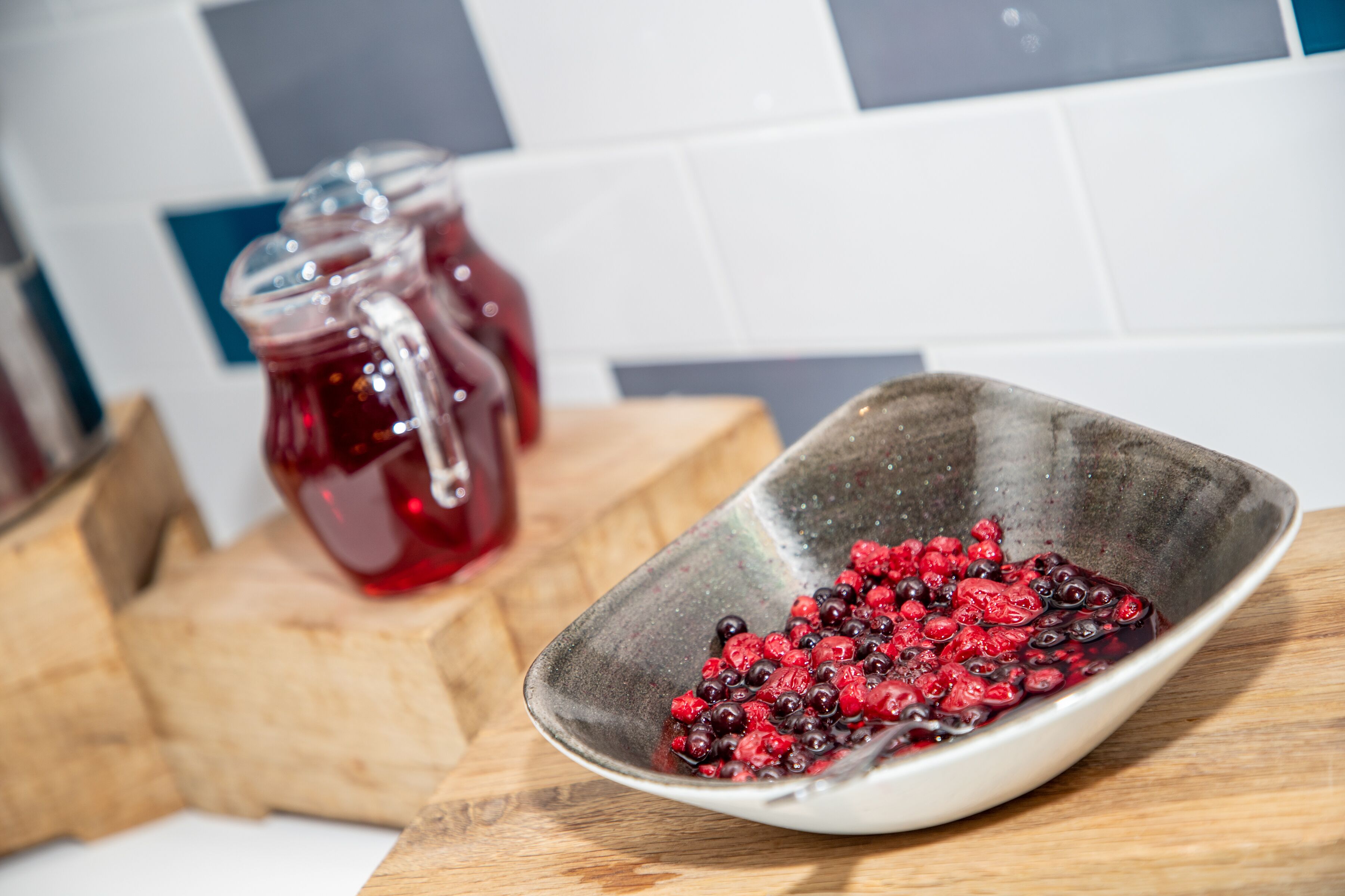 A kitchen counter with a bowl of berries and two glass jars in the background.