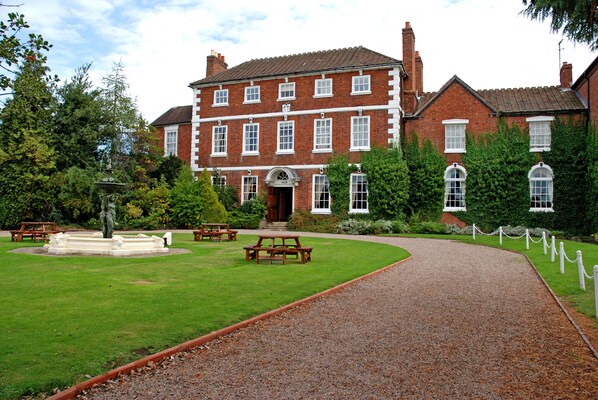 A large brick building with a central entrance, surrounded by a gravel path and picnic tables. - Park House Hotel (Shifnal)