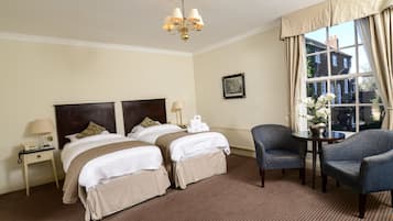 Habitación de hotel con dos camas, zona de estar con una mesa y sillas, candelabro y ventana con cortinas.