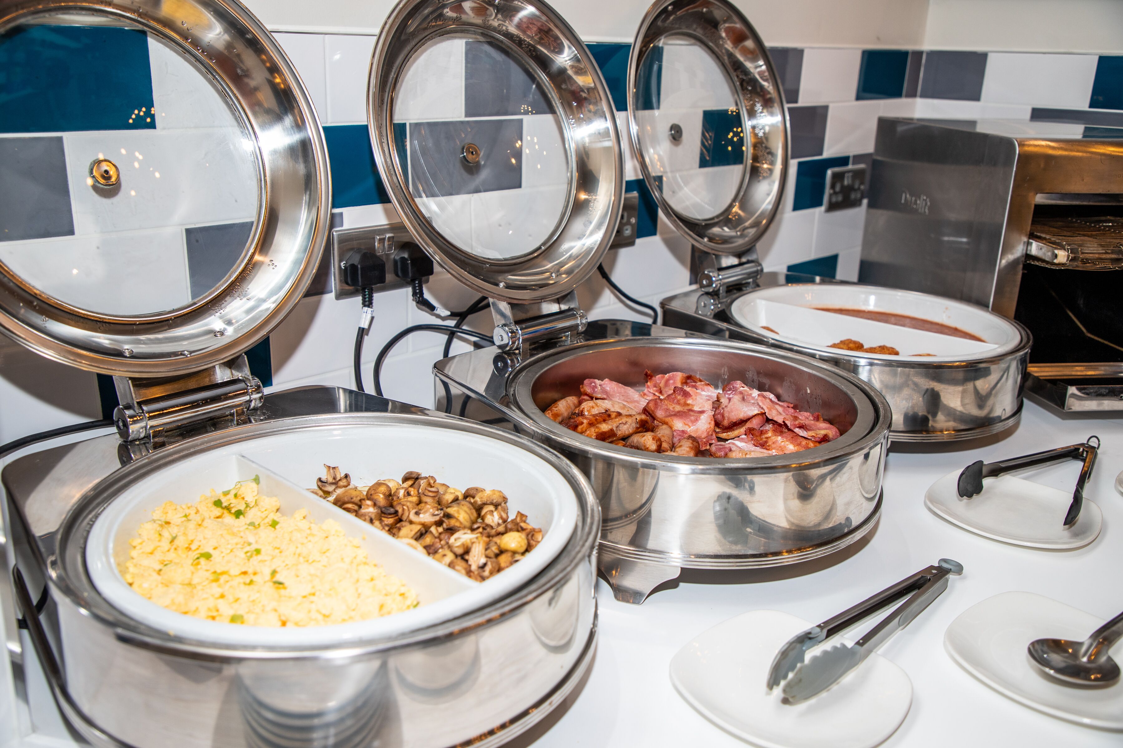 Ein reichhaltiges Buffet mit verschiedenen Speisen, darunter Rührei, Speck und Pilze.
