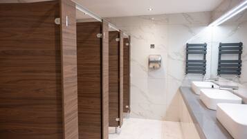 A modern bathroom with wooden stalls, marble walls, and a vanity with sinks and a mirror.