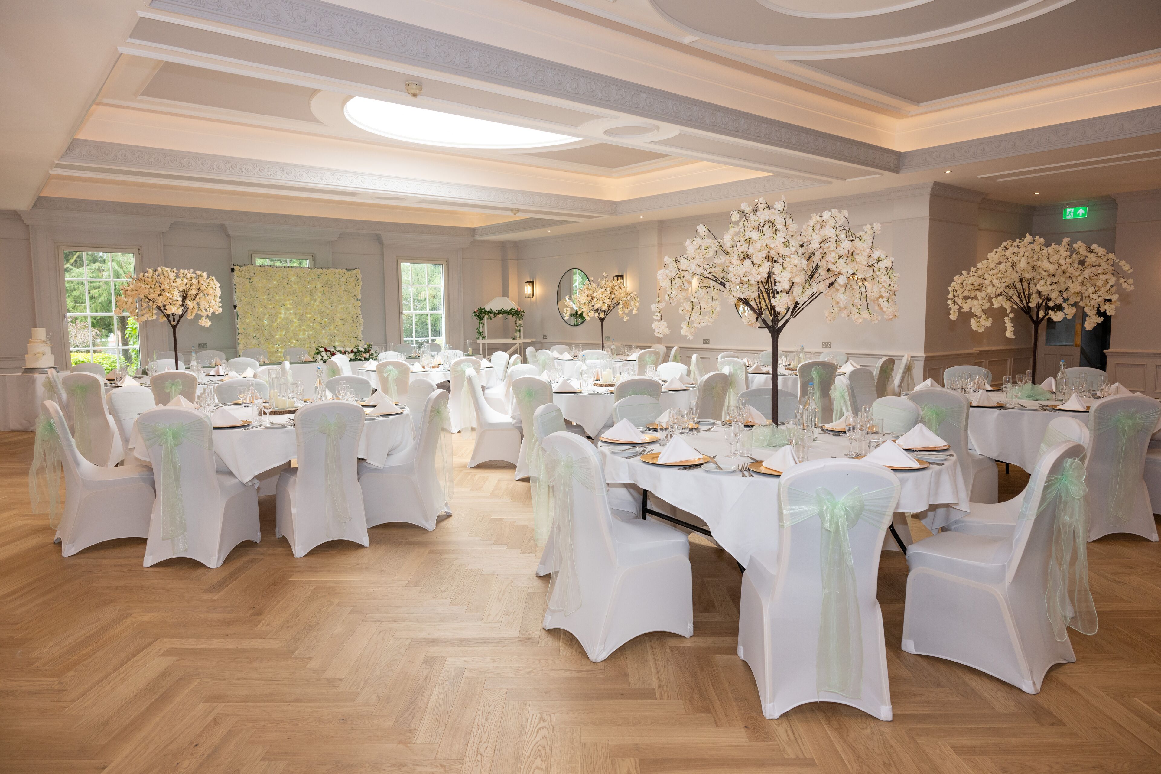 A banquet hall with round tables, white chairs, and floral centerpieces.