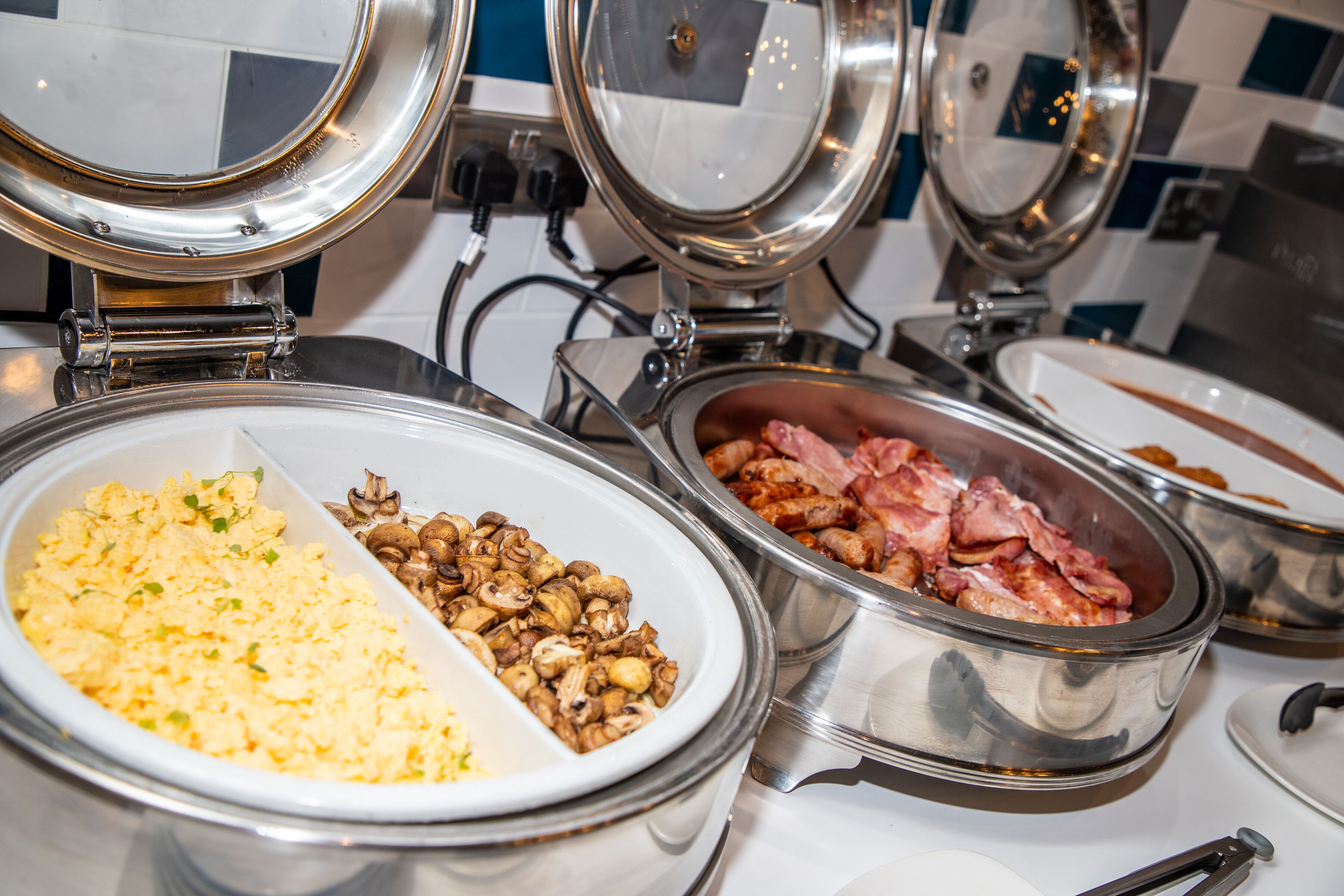A buffet with various food options including scrambled eggs, mushrooms, and ham.