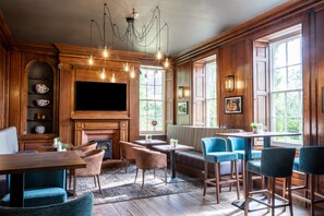 A cozy room with a fireplace, wooden walls, and a large window. There are chairs, a table, and a sofa. - Park House Hotel (Shifnal)