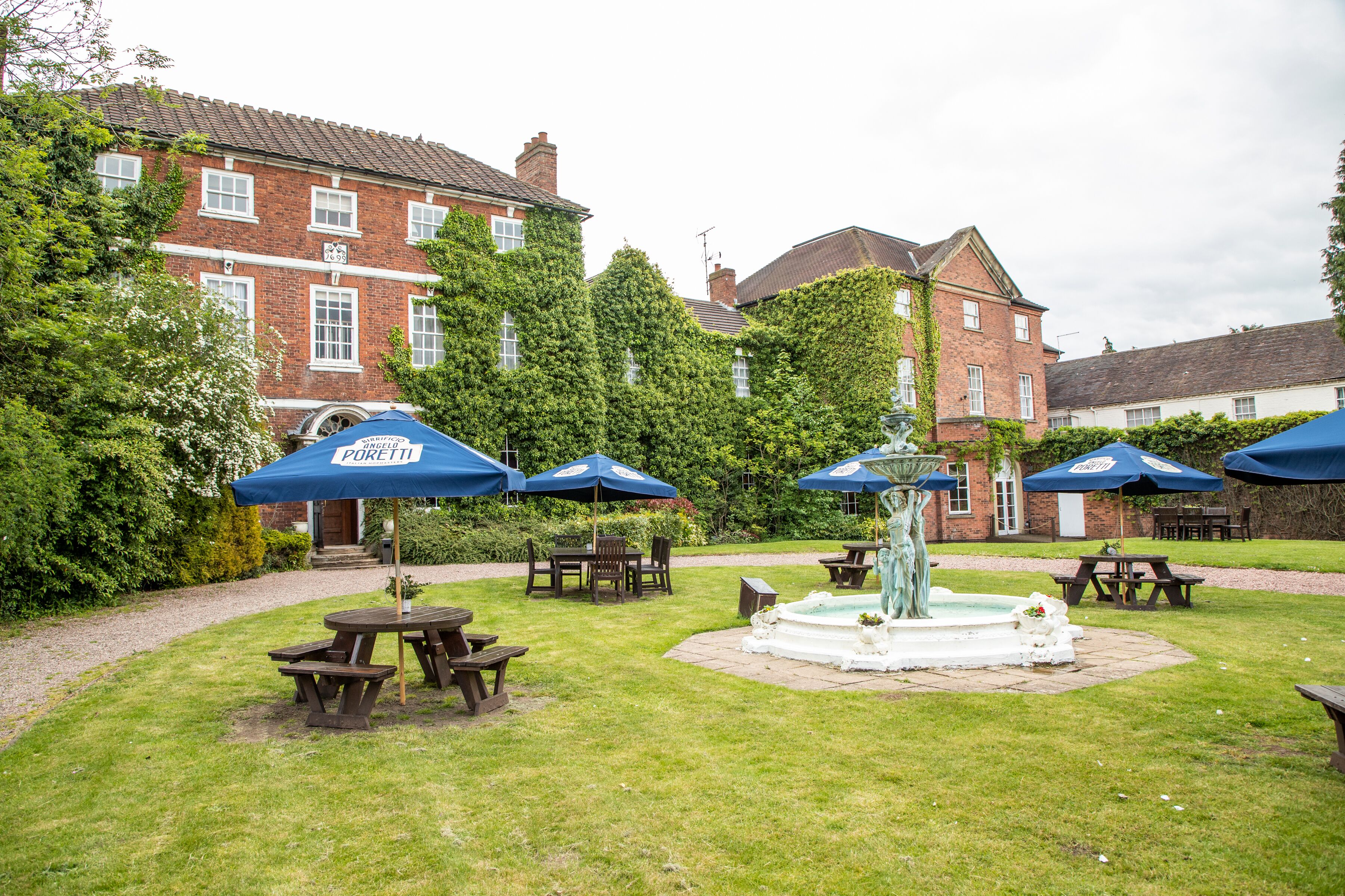A courtyard with picnic tables and blue umbrellas, a fountain, and a brick building in the background.