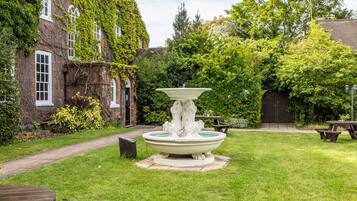 Une cour avec une fontaine, des tables de pique-nique et un bâtiment en briques recouvert de lierre.